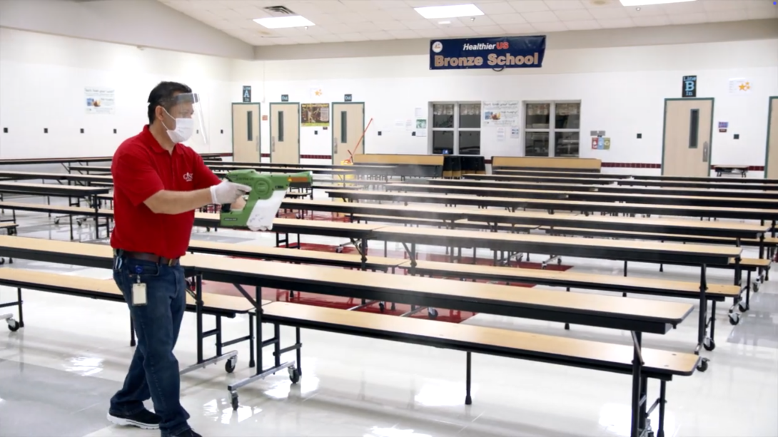 Custodian uses electrostatic disinfecting sprayer in cafeteria