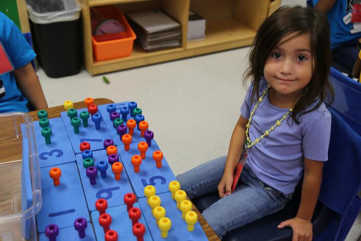 A prekindergartner smiles while working on a number puzzle.