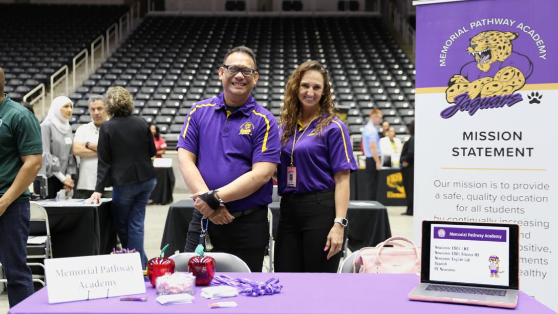 Two Memorial Pathway Academy staff members smile and pose for a photo behind their decorated table.