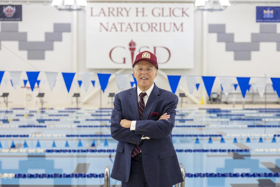 Man stands in front of pool and a large sign that reads Larry H. Glick Natatorium