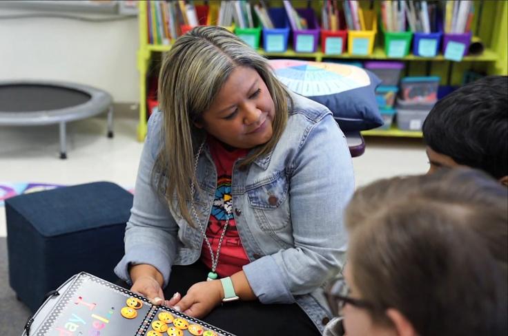 A teacher smiles while helping students used a mood chart.