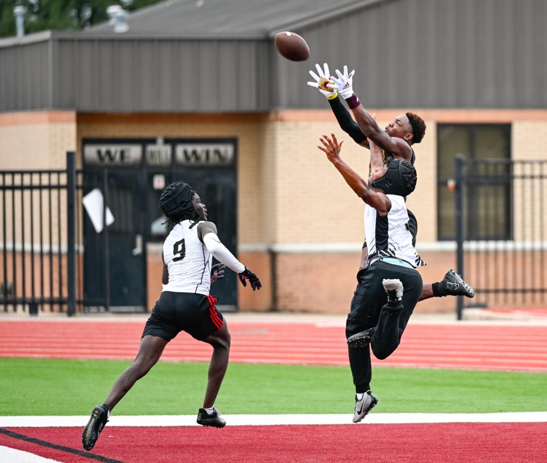 One football player jumps to catch the ball while two others try to block it.