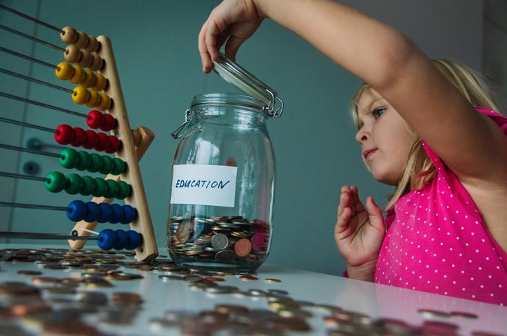 Young girl putting coins in jar labeled "education"