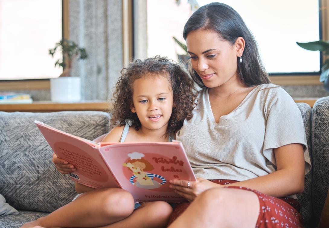 Mother and daughter sitting on couch looking at a book