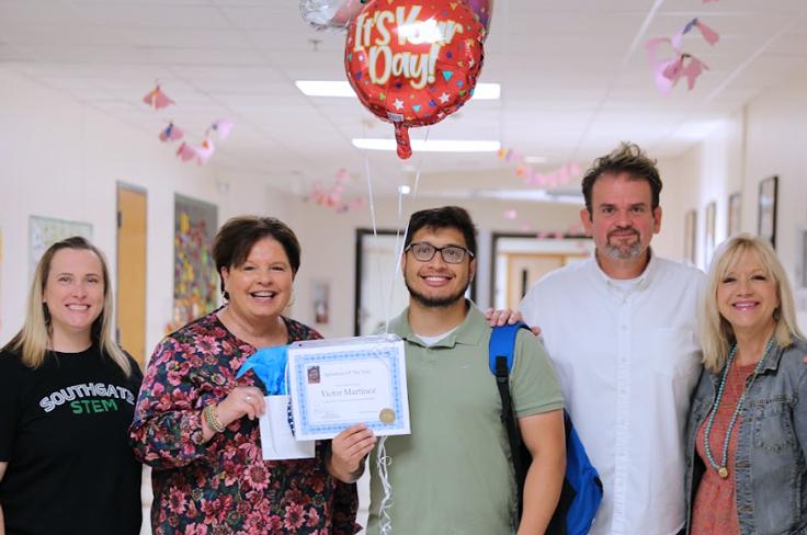 Smiling staff members with a substitute of the month winner holding a certificate and a balloon