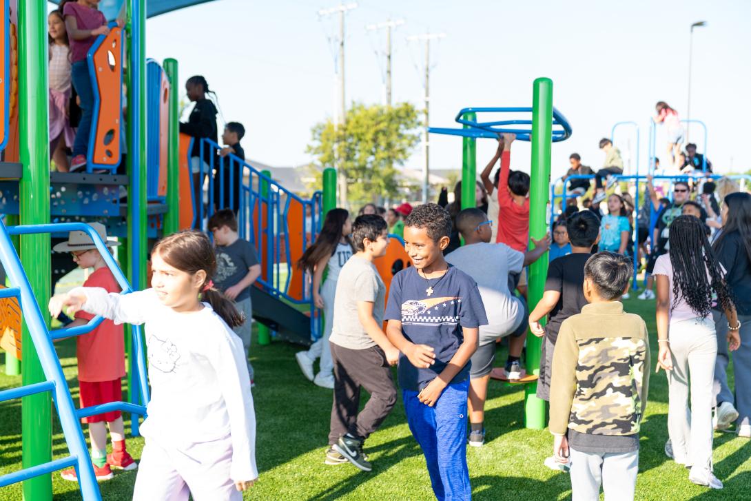 Several students walk around and play on the playground equipment