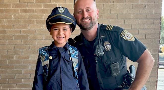 A School Resource Officer smiles with a student wearing an officer outfit.