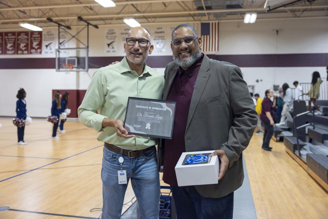 Two gentleman stand holding a gift box and a certificate