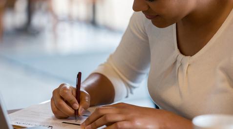 A student fills out an application, referencing her laptop.