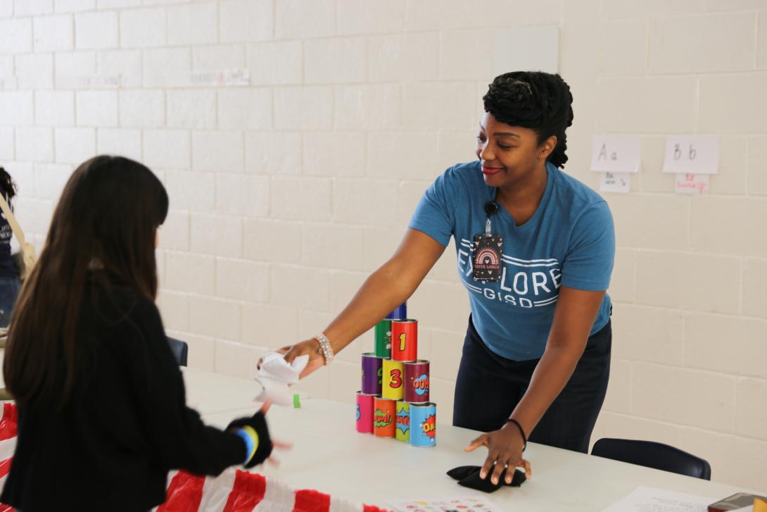 A female teacher hands an item to a student
