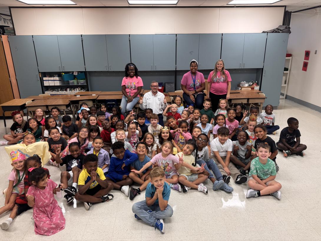 A large group of students sit with four adults kneeling behind them