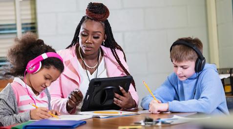 A teacher works with two students wearing assistive headphones.