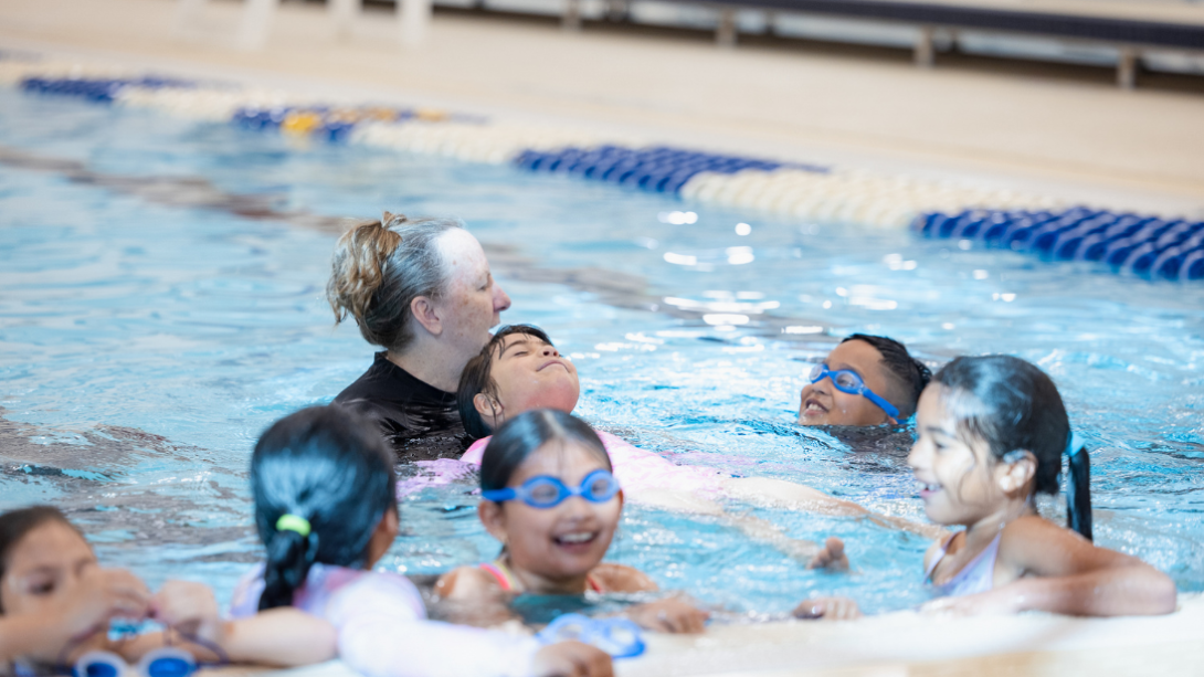 A water safety instructor assists students in the pool