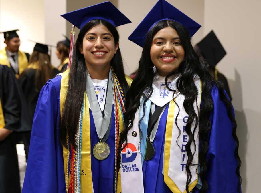 Two graduating girls in cap and gown with Dallas College stole.