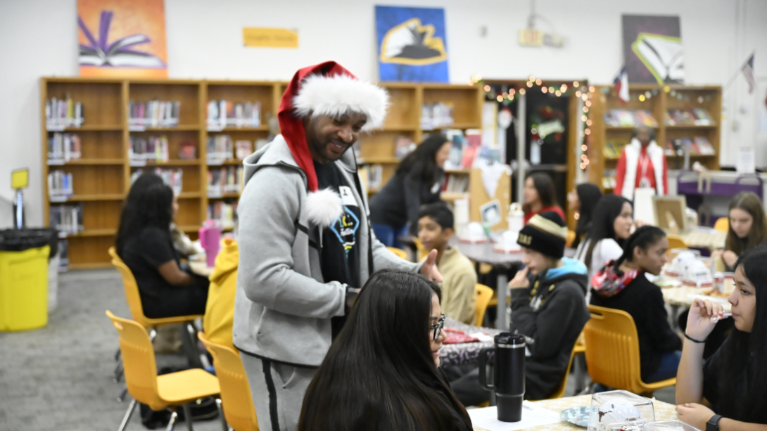 An adult man in a Santa hat speaks with a group of students