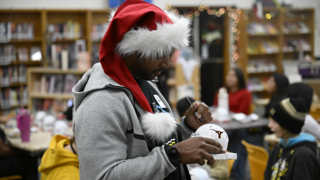 An adult man in a Santa hat signs a miniature football helmet