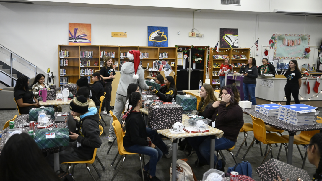 An adult man in a Santa hat distributes presents to a group of students