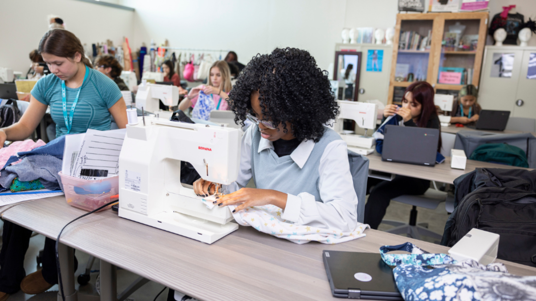 A group of students sit in rows using sewing machines