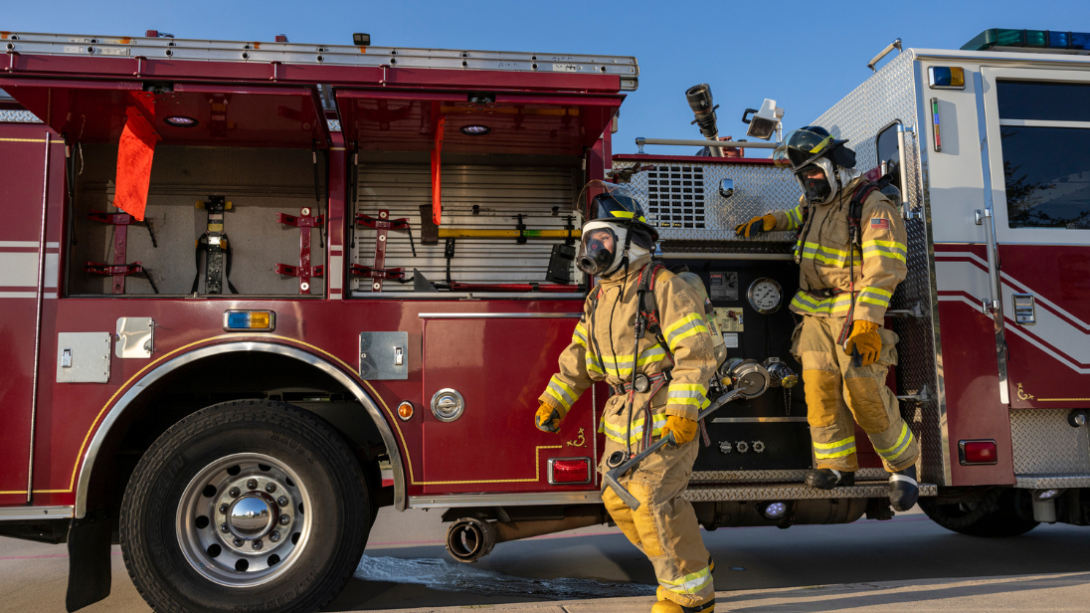 Two students in firefighting gear exit a fire truck