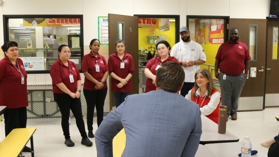cafeteria workers discuss food preparation with a man in a suit