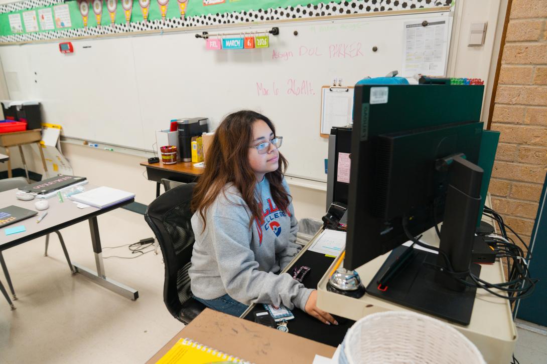 a female teacher sits at a desk with a computer