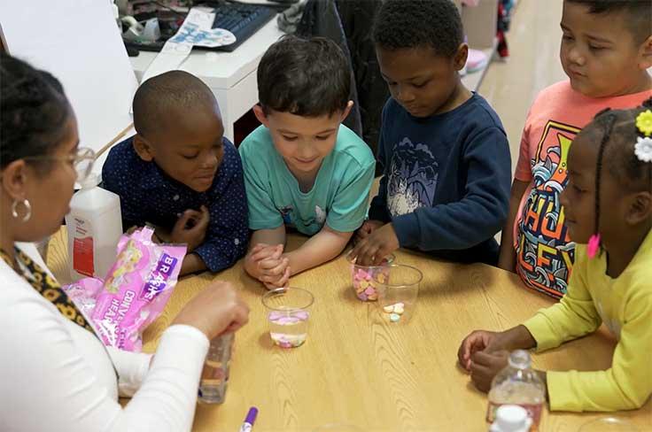 PreK students gathered around a table looking at a science experiment