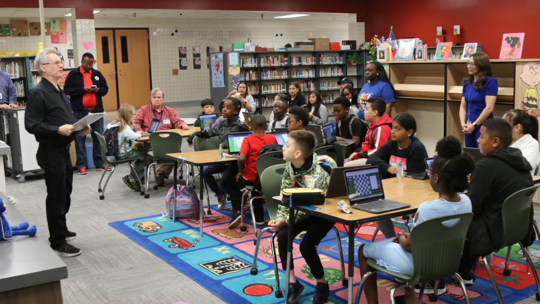 a diverse group of students sit while listening to an adult male speaker