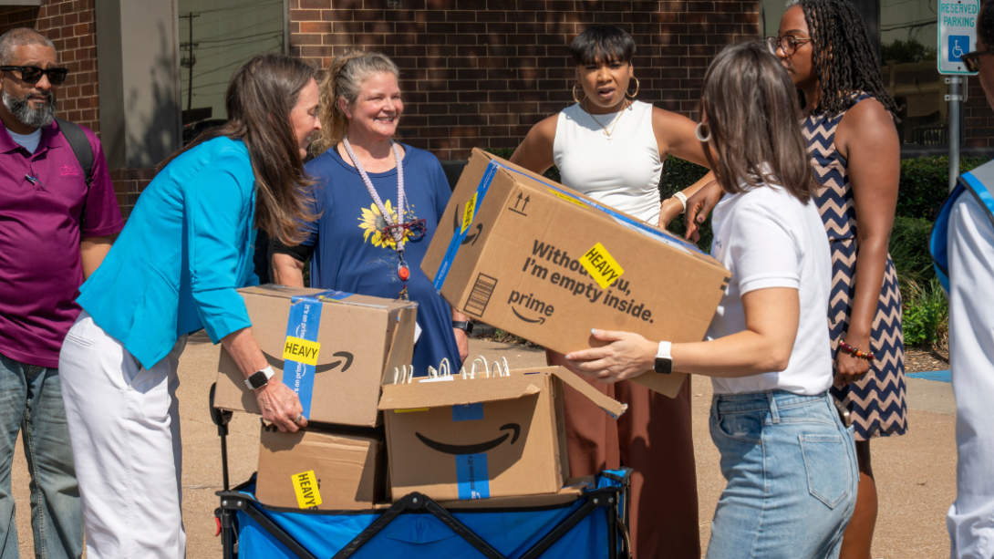 a group of adults stand around a wagon filled with cardboard boxes