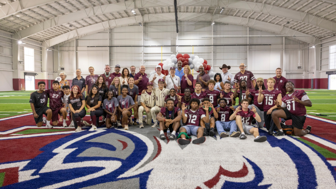 A diverse group of athletes, coaches, and staff pose for photo on an indoor field
